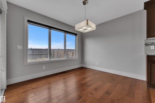 Open-concept space featuring wood-finish flooring, a contemporary ceiling light fixture, and a large window - 3363 13 Avenue, Edmonton, AB - Indoor Photo Showing Other Room