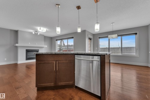 Kitchen island featuring dark wood cabinetry, a granite countertop, and a stainless steel dishwasher - 3363 13 Avenue, Edmonton, AB - Indoor Photo Showing Kitchen With Upgraded Kitchen