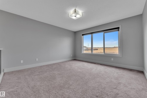 Carpeted room featuring a large window with a dark roller shade, light gray walls, white baseboards, and a flush-mount ceiling light fixture - 3363 13 Avenue, Edmonton, AB - Indoor Photo Showing Other Room