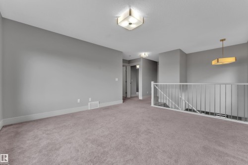 Spacious carpeted landing featuring a white railing, contemporary flush-mount lighting, a modern pendant light, and neutral wall tones - 3363 13 Avenue, Edmonton, AB - Indoor Photo Showing Other Room
