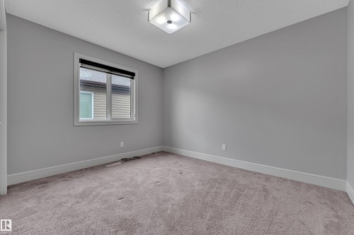 Neutral gray walls with white baseboards and trim, complemented by a window with a dark roller shade, and a flush-mount ceiling light fixture - 3363 13 Avenue, Edmonton, AB - Indoor Photo Showing Other Room