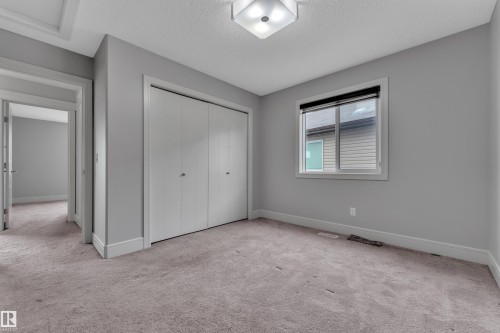 Room featuring soft gray wall paint, light-colored carpeting, a window with a dark roller blind, a built-in closet with bi-fold doors, and a ceiling-mounted light fixture - 3363 13 Avenue, Edmonton, AB - Indoor