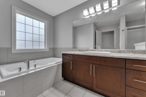 Spacious bathroom featuring a built-in soaking tub with chrome fixtures, a large privacy window, and a single vanity with a solid surface countertop - 3363 13 Avenue, Edmonton, AB - Indoor Photo Showing Bathroom