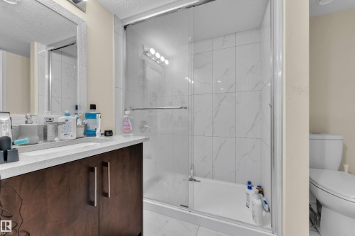 Bathroom featuring a combined tub and shower with glass enclosure, white tile surround, dark wood-finish vanity with a light-colored countertop, and a mirrored medicine cabinet - 3363 13 Avenue, Edmonton, AB - Indoor Photo Showing Bathroom