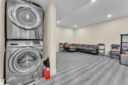 Stackable laundry appliances featuring a front-loading washer and dryer, recessed lighting, neutral wall paint, and wood-finish flooring - 3363 13 Avenue, Edmonton, AB - Indoor Photo Showing Laundry Room