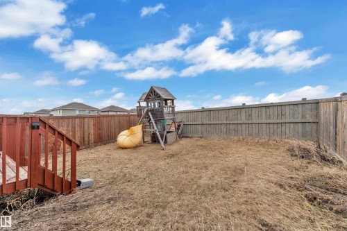 Expansive backyard with a wooden fence enclosing the perimeter, featuring a wooden deck with railing and a built-in play structure with a spiral slide - 3363 13 Avenue, Edmonton, AB - Outdoor