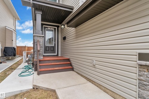 Front entry featuring a dark wood-finish door with upper glass panel, wood-finish steps, and a stone-clad column - 3363 13 Avenue, Edmonton, AB - Outdoor With Exterior