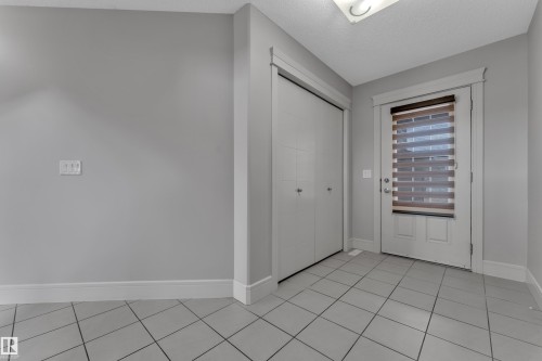 Entryway featuring light grey wall paint, white trim, square tile flooring, a built-in closet with double bifold doors, and an exterior door with a brown and white privacy blind - 3363 13 Avenue, Edmonton, AB - Indoor Photo Showing Other Room