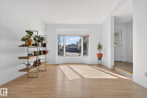 Bright living area featuring a prominent bay window, light wood-finish flooring, white baseboards, and neutral wall tones - 8403 190 Street, Edmonton, AB - Indoor Photo Showing Other Room
