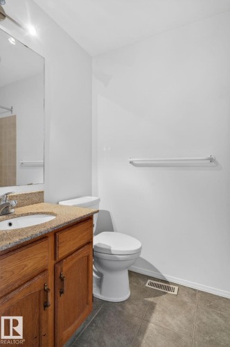 Bathroom featuring a wood-finish vanity with a built-in sink, granite-style countertop, and a large wall-mounted mirror - 8403 190 Street, Edmonton, AB - Indoor Photo Showing Bathroom