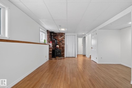Spacious finished basement featuring wood-finish flooring and a corner wood-burning stove with a brick surround - 8403 190 Street, Edmonton, AB - Indoor Photo Showing Other Room