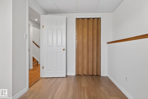 Room featuring wood-finish flooring, a white panel door, and a light wood accordion-style door - 8403 190 Street, Edmonton, AB - Indoor Photo Showing Other Room