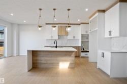 Modern kitchen featuring a large central island with a waterfall countertop, light wood-finish cabinetry, and white overhead cabinets with matte black hardware - 