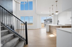 Two-story living space featuring an open-concept design with light wood-finish flooring, a contemporary staircase with carpeted treads and black metal railings, and a kitchen island with a white countertop and wood-finish paneling - 
