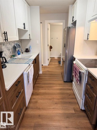 Kitchen featuring wood-finish flooring, white upper cabinetry with matte black hardware, and wood-finish lower cabinetry - 106 10725 111 Street, Edmonton, AB - Indoor Photo Showing Kitchen