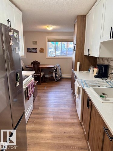Kitchen featuring wood-finish flooring, white and wood-finish cabinetry with matte black hardware, white countertops, and a stainless steel refrigerator - 106 10725 111 Street, Edmonton, AB - Indoor Photo Showing Kitchen