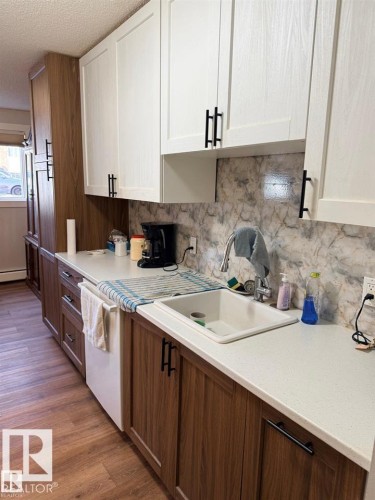 Kitchen featuring two-tone cabinetry with white upper cabinets and wood-finish lower cabinets, black hardware, solid surface countertops, and a full backsplash - 106 10725 111 Street, Edmonton, AB - Indoor Photo Showing Kitchen