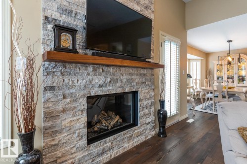 Stone veneer fireplace with a substantial wood mantel, a built-in gas insert, and wood-finish flooring - 47 1130 Falconer Road, Edmonton, AB - Indoor Photo Showing Living Room With Fireplace