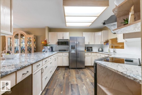 Kitchen featuring extensive stone countertops, light-toned cabinetry, stainless steel appliances, and wood-finish flooring - 47 1130 Falconer Road, Edmonton, AB - Indoor Photo Showing Kitchen
