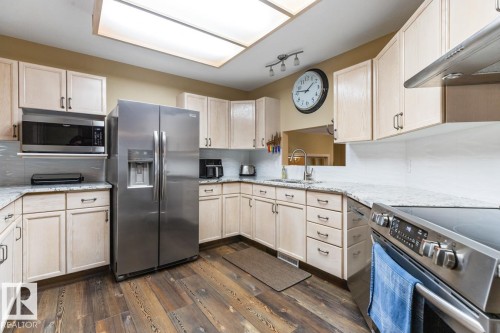 Kitchen featuring wood-finish flooring, light-toned cabinetry, stainless steel appliances, and light-colored countertops - 47 1130 Falconer Road, Edmonton, AB - Indoor Photo Showing Kitchen