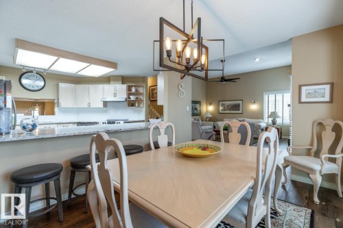Dining area with a modern linear chandelier, wood-finish flooring, and direct sightlines to the kitchen - 47 1130 Falconer Road, Edmonton, AB - Indoor Photo Showing Dining Room