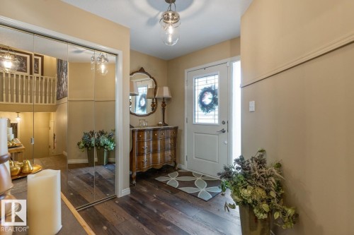 Entryway featuring wood-finish flooring, a white front door with decorative glass inserts and a sidelight, and a full-length mirrored closet door - 47 1130 Falconer Road, Edmonton, AB - Indoor Photo Showing Other Room