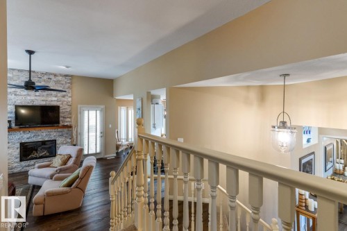 Living area featuring a floor-to-ceiling stacked stone fireplace with a wood mantle, a ceiling fan, and dark wood-finish flooring - 47 1130 Falconer Road, Edmonton, AB - Indoor Photo Showing Other Room With Fireplace
