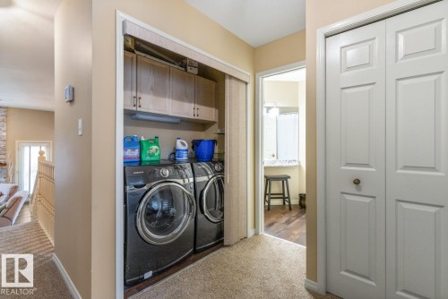 Laundry area featuring a stackable washer and dryer, upper cabinetry for storage, and a folding door closet - 47 1130 Falconer Road, Edmonton, AB - Indoor Photo Showing Laundry Room
