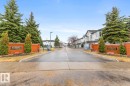 Community entrance featuring brick signage with metal lettering, mature evergreen trees, and manicured shrubs - 47 1130 Falconer Road, Edmonton, AB  - Outdoor 