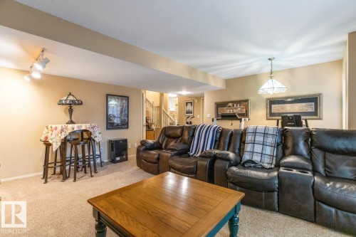 Carpeted living area featuring track lighting, a central hanging fixture, and a stairway entry - 47 1130 Falconer Road, Edmonton, AB - Indoor Photo Showing Living Room