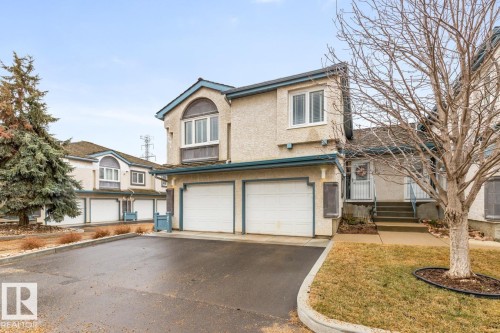 Exterior showcasing a two-car garage with white doors, a stucco finish, and a prominent arched window on the upper level - 47 1130 Falconer Road, Edmonton, AB - Outdoor With Facade