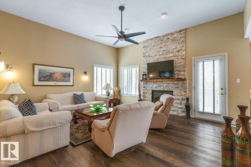Spacious living area featuring high vaulted ceilings, rich wood-finish flooring, a contemporary ceiling fan, and a floor-to-ceiling stacked stone fireplace with a wood mantle - 47 1130 Falconer Road, Edmonton, AB - Indoor Photo Showing Living Room With Fireplace