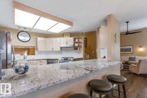 Kitchen featuring a granite countertop island with seating, stainless steel appliances, light-toned cabinetry, a white tile backsplash, and recessed ceiling lighting - 47 1130 Falconer Road, Edmonton, AB - Indoor Photo Showing Kitchen With Upgraded Kitchen