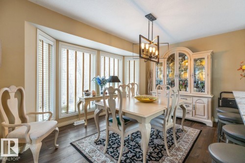 Dining area featuring wood-finish flooring, a contemporary linear chandelier, and a bay window with multiple panes - 47 1130 Falconer Road, Edmonton, AB - Indoor Photo Showing Dining Room