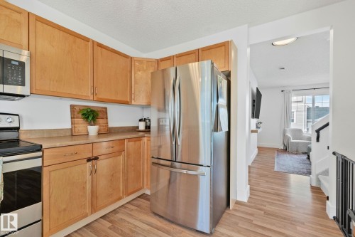 Kitchen featuring wood-finish flooring, ample wood cabinetry, a stainless steel French door refrigerator, and stainless steel microwave - 53 2503 24 Street, Edmonton, AB - Indoor Photo Showing Kitchen