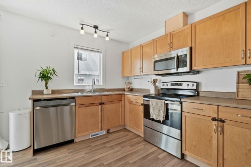 Kitchen featuring wood cabinetry, stainless steel appliances, a corner sink, and wood-finish flooring - 53 2503 24 Street, Edmonton, AB - Indoor Photo Showing Kitchen With Stainless Steel Kitchen