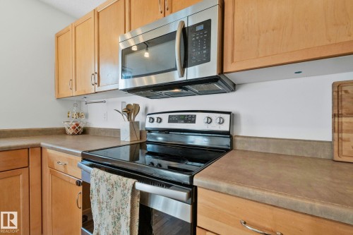 Kitchen featuring light wood cabinetry, a stainless steel over-the-range microwave, a black electric range with a stainless steel oven door, solid surface countertops, and white walls - 53 2503 24 Street, Edmonton, AB - Indoor Photo Showing Kitchen