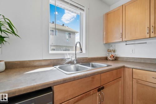 Kitchen featuring a double basin stainless steel sink with a high-arc faucet, light wood-finish cabinetry, and solid surface countertops - 53 2503 24 Street, Edmonton, AB - Indoor Photo Showing Kitchen With Double Sink