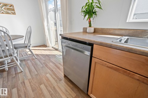 Kitchen area featuring wood-finish flooring, light wood cabinetry, a stainless steel dishwasher, a built-in sink, and a sliding glass door leading to the exterior - 53 2503 24 Street, Edmonton, AB - Indoor Photo Showing Kitchen