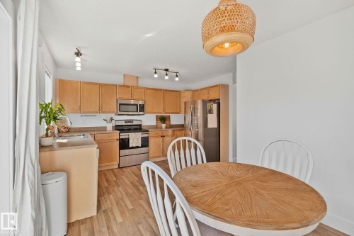 Bright kitchen featuring light wood cabinetry, stainless steel appliances, wood-finish flooring, and track lighting - 53 2503 24 Street, Edmonton, AB - Indoor