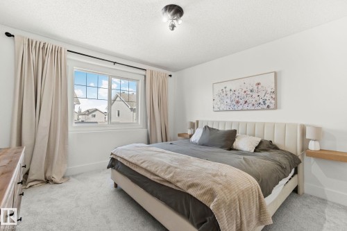 Bright bedroom featuring a large window with grid pattern, light-toned carpeting, and neutral wall tones - 53 2503 24 Street, Edmonton, AB - Indoor Photo Showing Bedroom