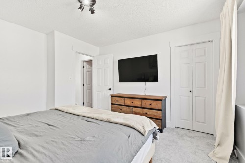 Carpeted bedroom featuring white walls, track lighting, a bi-fold closet door, and a six-drawer dresser with a mounted television above - 53 2503 24 Street, Edmonton, AB - Indoor Photo Showing Bedroom