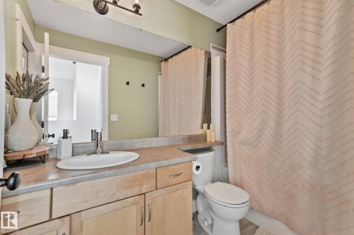 Bathroom featuring a vanity with wood-finish cabinetry, a single basin sink, a large mirror, a toilet, and a shower/tub combination with a patterned curtain - 53 2503 24 Street, Edmonton, AB - Indoor Photo Showing Bathroom