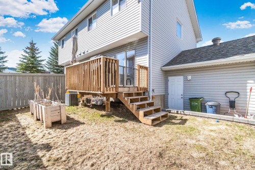 Rear exterior featuring a wood deck with stairs, vinyl siding, a privacy fence, a raised garden bed, and a lower-level access door - 53 2503 24 Street, Edmonton, AB - Outdoor With Deck Patio Veranda With Exterior