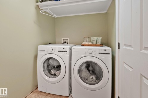 Dedicated laundry area featuring front-loading washer and dryer units, a wall-mounted shelf, and light-toned wall paint - 53 2503 24 Street, Edmonton, AB - Indoor Photo Showing Laundry Room