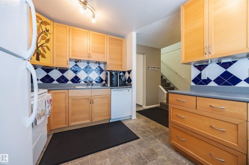 The kitchen features light wood cabinetry, blue and white tiled backsplash, and durable tile flooring - Sherwood Park, AB - Indoor Photo Showing Kitchen
