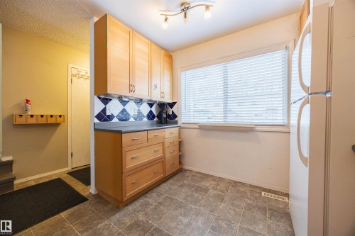 Kitchen area featuring light wood cabinetry, a dark countertop, and decorative blue and white tile backsplash - Sherwood Park, AB - Indoor