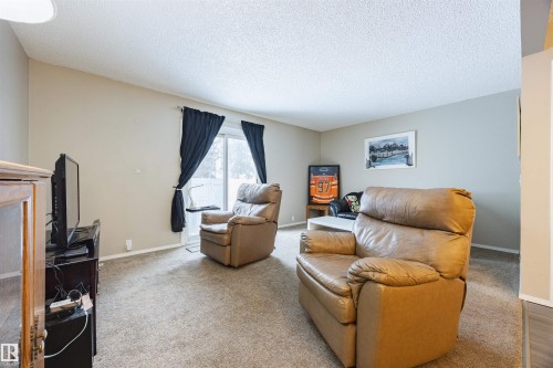 The living area features neutral-toned walls, carpeted flooring, and a sliding glass door with dark curtains - Sherwood Park, AB - Indoor