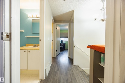 The property features grey wood-style flooring, a white staircase, and a bathroom with a vanity, mirror, and light fixture - Sherwood Park, AB - Indoor Photo Showing Other Room