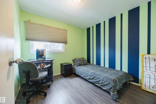 Room featuring light green and striped accent walls, a window with blinds, and wood-look flooring - Sherwood Park, AB - Indoor Photo Showing Bedroom